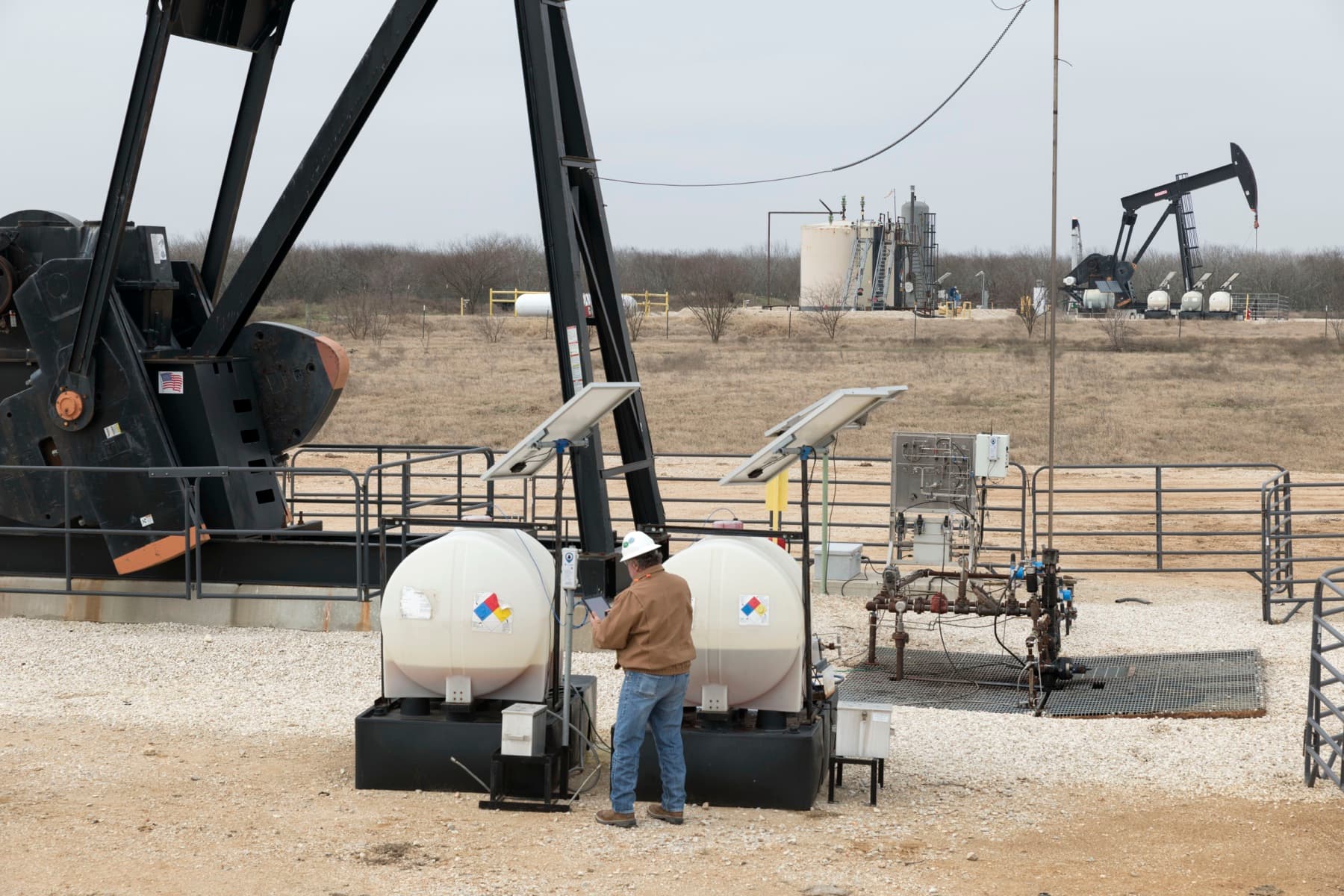 Field technician standing between chemical tanks and a pumpjack installation.