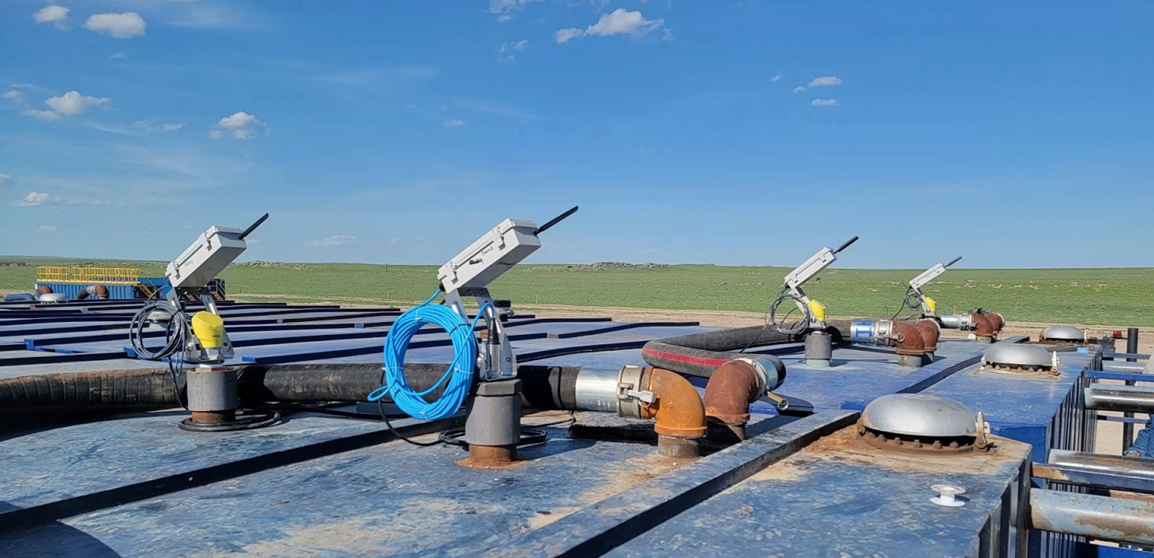 WellAware wireless radar level sensors mounted on a row of frac tanks at an open-prairie well site
